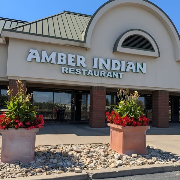 Exterior of Amber Indian Restaurant with large planters of red flowers flanking the entrance.