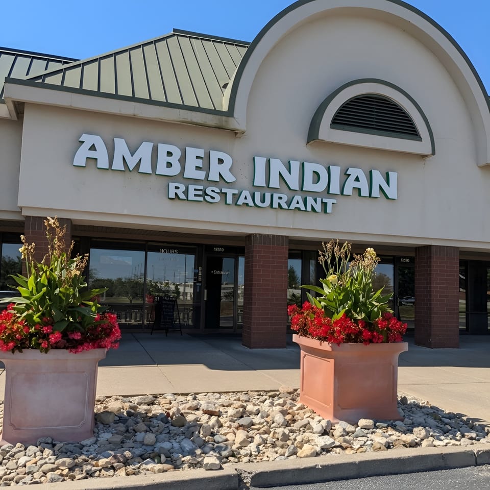 Exterior of Amber Indian Restaurant with large planters of red flowers flanking the entrance.