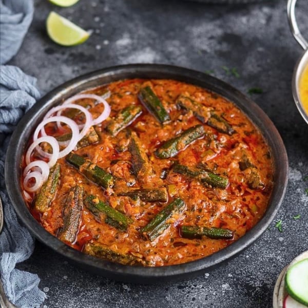 Indian bhindi masala, a spicy okra curry, garnished with onion rings and lime wedges.