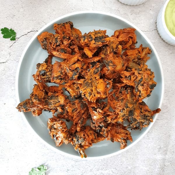 A light blue plate filled with crispy, golden-brown pakoras, garnished with a sprig of cilantro.