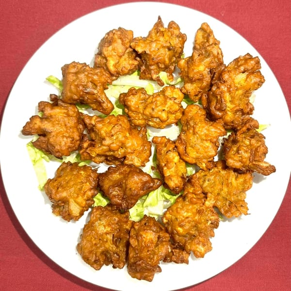 A white plate filled with golden-brown fried pakora pieces on a bed of lettuce, against a red tablecloth.
