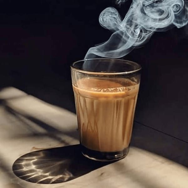 Steaming glass of chai tea on a light surface with a dark background.