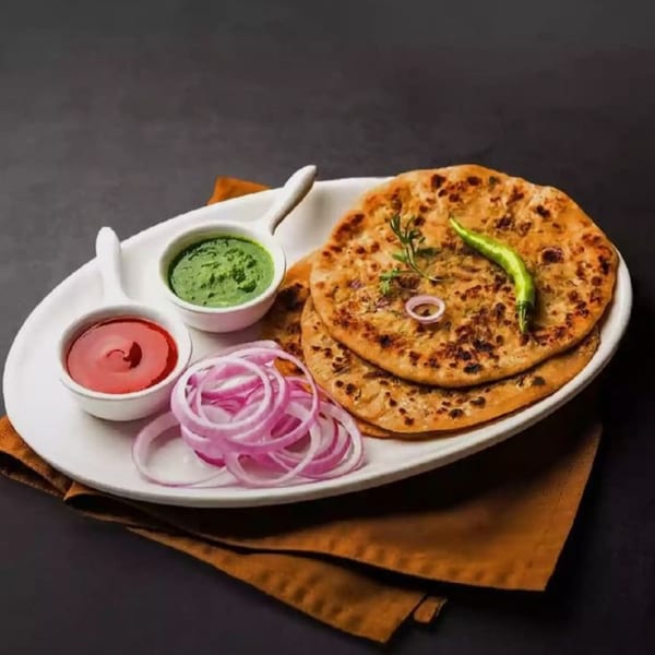 Golden-brown parathas with green chutney, red sauce, and sliced red onions on a white plate.